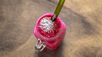 Roze smoothie met een groene rietje en witte topping op een houten oppervlak.