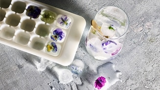 IJsblokjes met bloemen in een ijsblokjeshouder en een glas water met bloeiende ijsblokjes.