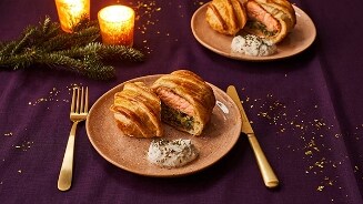 Feestelijke maaltijd van zalm en bladerdeeg op een bord, geserveerd met een kruidensaus, met een sfeervolle achtergrond van kaarslicht en dennentakken.