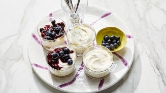 Bord met glazen gevuld met yoghurt en bosbessen, geserveerd op een marmeren tafel.