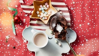 Chocolade lava cake met warme chocolademelk en marshmallows op een kerstthema tafelkleed.