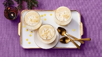 Drie glazen dessert op een dienblad met gouden sterren, geserveerd met gouden lepels en een kaars op een paarse achtergrond.
