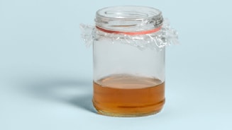 Glazen pot met amberkleurige vloeistof en plastic folie als deksel.
