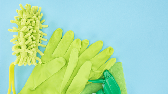 Schoonmaakset met gele schoonmaakhandschoenen, een schoonmaakdoekje, een verstuiver en een stofdoek op een blauwe ondergrond