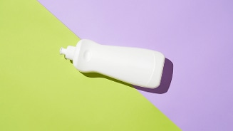 Witte plastic fles op een ondergrond met groen en paars, mogelijk voor schoonmaakmiddel of afwasmiddel.