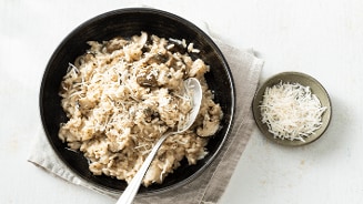 Risotto met champignons en geraspte Parmezaanse kaas in een zwarte kom, naast een schaaltje extra kaas.