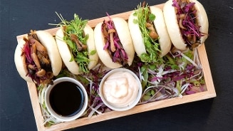 Gestoomde bao buns gevuld met paddenstoelen, verse groenten en kruiden, geserveerd met sojasaus en een romige dipsaus op een houten dienblad