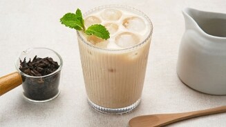 Glas iced chai latte met muntblaadjes, naast losse zwarte thee en een melkkan.