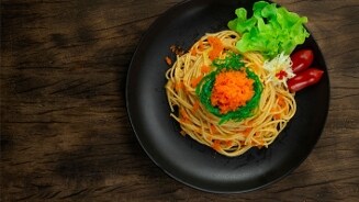 Spaghetti met salade en tomaatjes op een zwart bord.