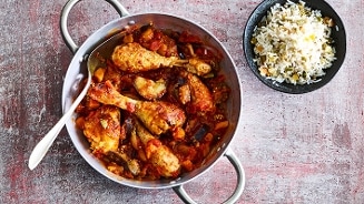 Gestoofd kipgerecht met groenten in tomatensaus, geserveerd met een kom rijst.