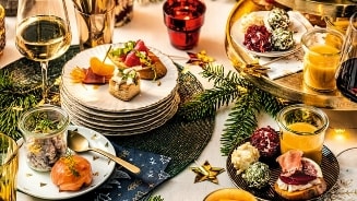 Feestelijke tafel met verschillende hapjes en glazen witte en rode wijn, omringd door decoraties en kerstversiering.