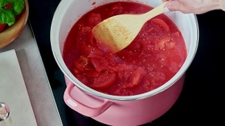 Tomatensaus wordt geroerd in een roze pan op het fornuis.
