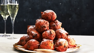 Oliebollen met krenten en rozijnen op een schaal, geserveerd met twee glazen champagne op de achtergrond.