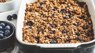 Havermout crumble met blauwe bessen in een ovenschaal, naast een kom verse blauwe bessen