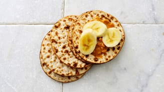 Knapperige ronde crackers met pindakaas en bananenplakjes op een marmeren oppervlak.