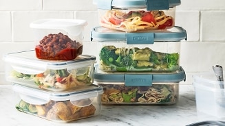 Plastic opbergbakken gevuld met diverse maaltijden, waaronder pasta en groenten, op een keukenblad.