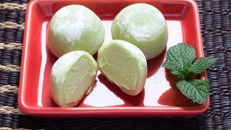 Groene mochi-ijs op een rood bord met muntblaadjes.