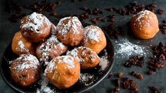 Oliebollen met poedersuiker op een bord, omringd door losse rozijnen