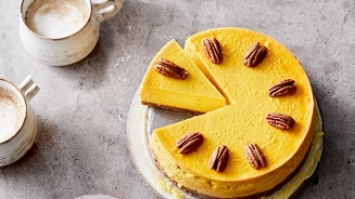Pompoen cheesecake met pecannoten, geserveerd met twee kopjes koffie.