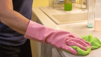Persoon met roze schoonmaakhandschoen die een keukenblad schoonmaakt met een groene doek.
