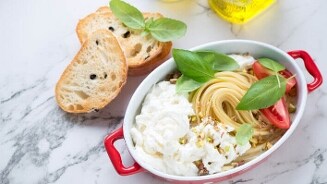 Pasta met burrata, tomaten en verse basilicum, geserveerd met knapperig stokbrood in een rode ovenschaal.