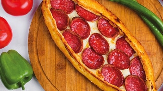 Pide met peperoni op een houten snijplank, omringd door rode en groene paprika's.