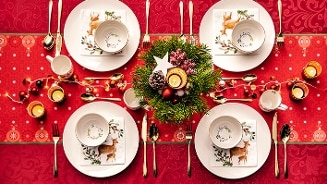 Feestelijk gedekte tafel met kerstdecoratie, servies met rendiermotief en een kerststuk in het midden.