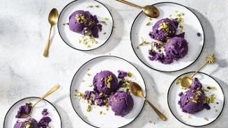 Verschillende borden met paarse ijsbolletjes, gegarneerd met stukjes pistache en goudkleurige lepels ernaast.