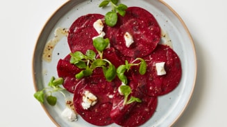 Bord met rode bieten carpaccio, gegarneerd met geitenkaas en verse kruiden.