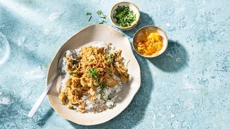 Curry met rijst en verse koriander, geserveerd met bijgerechten in kleine schaaltjes.