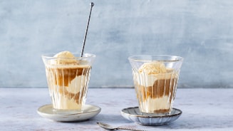 Twee glazen met affogato: vanille-ijs overgoten met espresso, geserveerd op schoteltjes met een lepeltje.