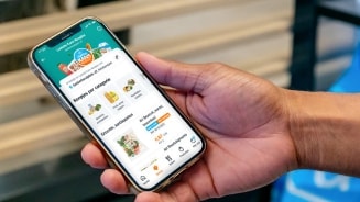 Hand houdt smartphone vast met Albert Heijn app geopend op het scherm, waarop verschillende boodschappen en aanbiedingen te zien zijn.