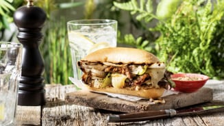 Broodje met vlees, uien en groene paprika op een houten plank met een glas citroenwater en een molen op de achtergrond.