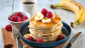 Pannenkoeken met schijfjes banaan, frambozen en siroop op een bord, met verse frambozen en een banaan op de achtergrond