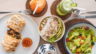 Ontbijttafel met wraps gevuld met groenten en bonen, havermoutbowl met fruit en noten, groene smoothie, sinaasappelsap en frisse gemengde salade