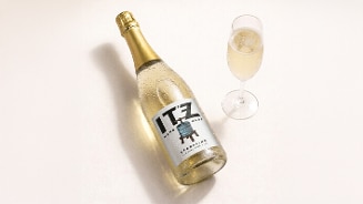 Fles ITZ Sparkling mousserende wijn met een gevuld champagneglas ernaast op een lichte ondergrond.