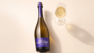 Fles Saboritz Spumante naast een glas mousserende wijn op een lichte achtergrond.