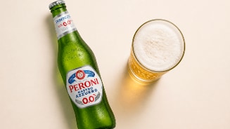 Fles Peroni Nastro Azzurro 0.0% alcoholvrije bier naast een glas gevuld met schuimend bier.