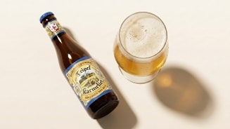 Fles Tripel Karmeliet en een glas blond bier met schuimkraag op een lichte ondergrond.