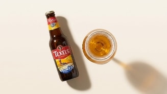 Fles Texels Skuumkoppe 0.0% alcoholvrij speciaalbier naast een glas gevuld met bier op een lichte achtergrond.