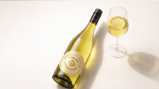 Fles Grange de Malverne Chardonnay met een glas witte wijn op een lichtgekleurde ondergrond.