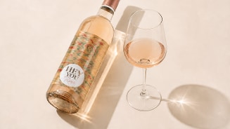 Fles rose Hey you Rosé naast een gevuld wijnglas op een lichte ondergrond.