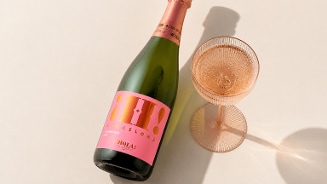 Fles rose Cava ¡Hola! Cava Brut Pink Bio naast een gevuld wijnglas op een lichte ondergrond.