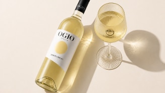 Fles witte wijn Ogio Pinot Grigio naast een gevuld wijnglas op een lichte ondergrond.