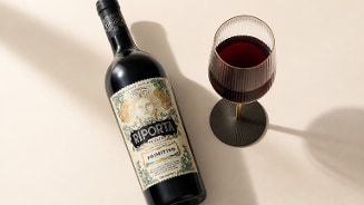 Fles rode wijn Riporta Primitivo naast een gevuld wijnglas op een lichte ondergrond.
