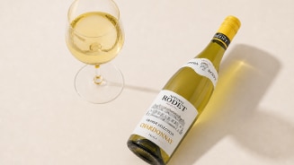 Fles witte wijn Rodet Grande Selection Chardonnay naast een gevuld wijnglas op een lichte ondergrond.