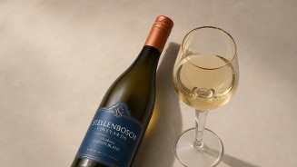Fles witte wijn Stellenbosch Vineyards Chenin Blanc naast een gevuld wijnglas op een lichte ondergrond.
