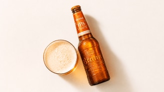 Fles Brand IPA bier naast een gevuld glas bier op een lichte ondergrond