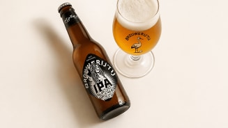 Flesje Brouwerij 't IJ IPA met daarnaast een ingeschonken glas bier.