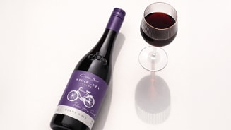 Fles rode wijn Cono Sur Bicicleta Pinot Noir naast een gevuld wijnglas op een lichte ondergrond.